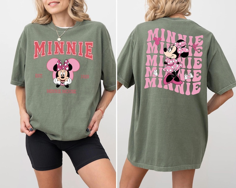 May include: Olive green t-shirt featuring a Minnie Mouse graphic. The front design includes the word "MINNIE" in pink, with a Minnie Mouse illustration below. The back of the shirt has a repeating pink "MINNIE" design with a Minnie Mouse illustration.