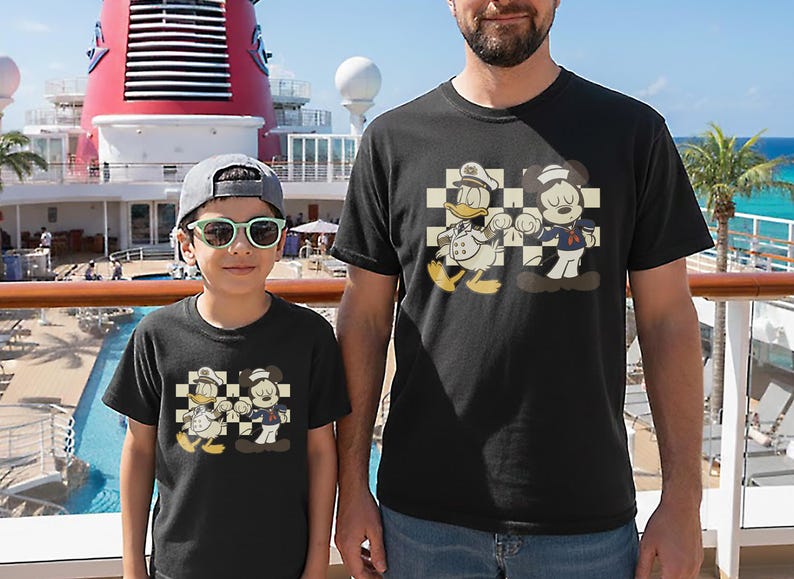 May include: Black t-shirts featuring a cartoon graphic of Donald Duck and Mickey Mouse in sailor and captain outfits. The characters are set against a checkered background. The shirts are worn by a child and an adult.