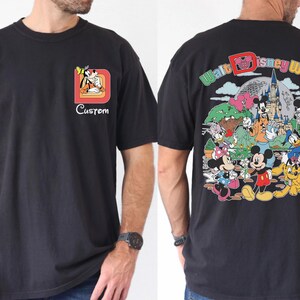 May include: Black t-shirt featuring a colorful Walt Disney World graphic on the back and a smaller Goofy design with the word "Custom" on the front. The shirt has a classic crew neck and short sleeves.