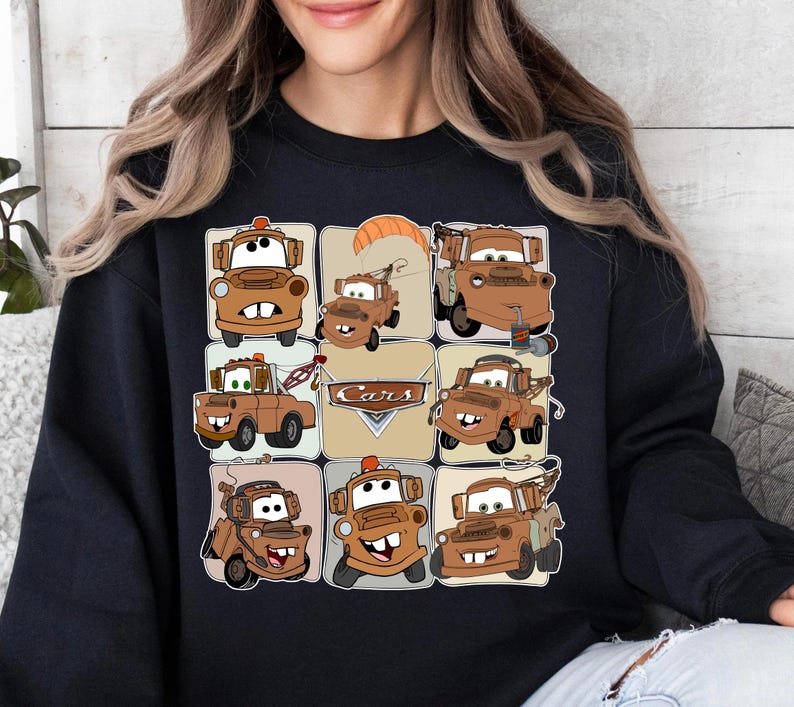 Może przedstawiać: Czarna bluza z nadrukiem w kratkę przedstawiającym postać Złomka z filmu Auta. Obrazy są w odcieniach brązu i beżu, z napisem "Cars" pośrodku.