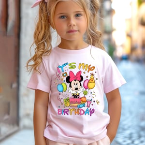 May include: A light pink t-shirt featuring a Minnie Mouse graphic with a pink bow, surrounded by birthday-themed elements. The text "It's my birthday" is displayed in colorful letters.