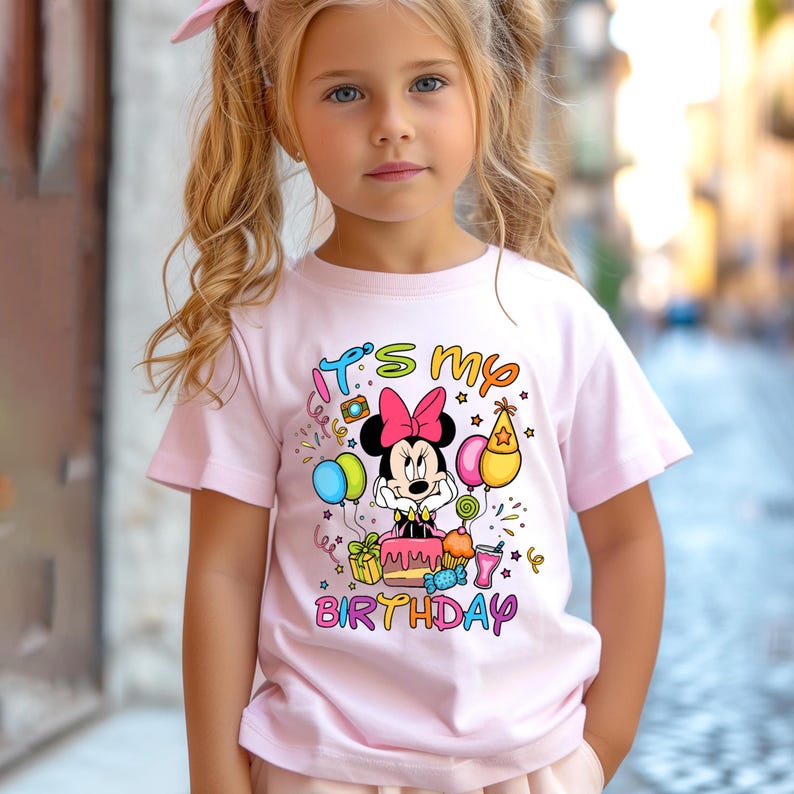 May include: A light pink t-shirt featuring a Minnie Mouse graphic with a pink bow, surrounded by birthday-themed elements. The text "It's my birthday" is displayed in colorful letters.