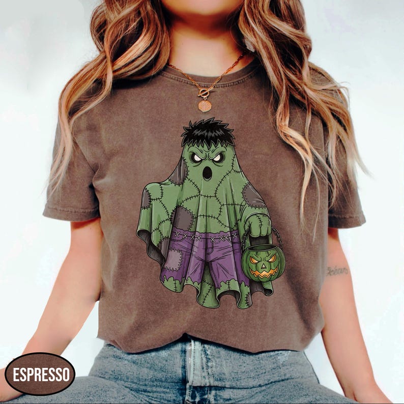 Op de afbeelding: Espresso-kleurig T-shirt met een Halloween-thema. Het ontwerp toont een groene geest met een Frankenstein-achtige uitstraling, een paarse broek en een pompoen-lantaarn. Het shirt is casual kleding.