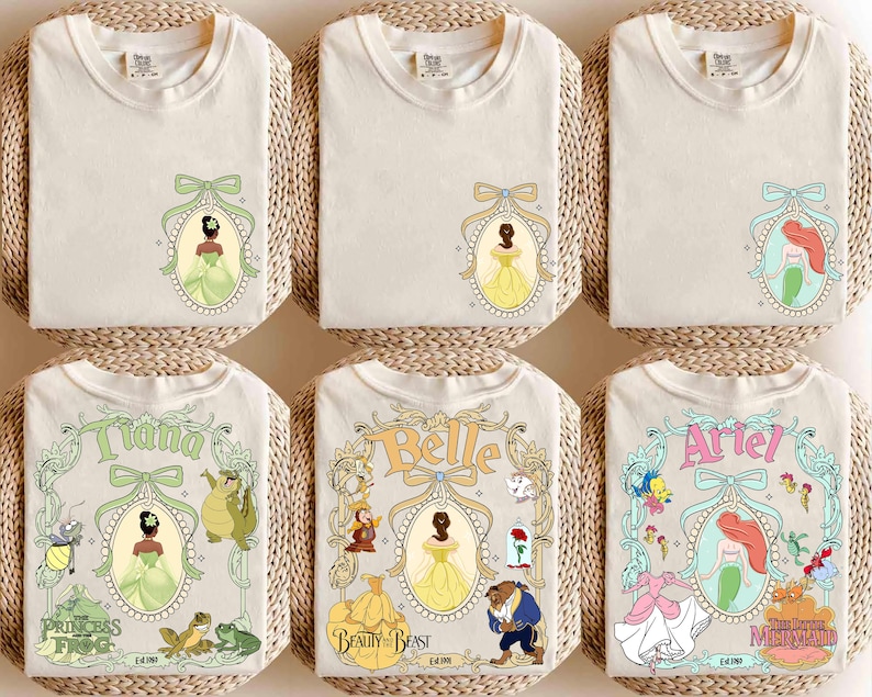 May include: Off-white t-shirts featuring Disney princess designs. The shirts display images of Tiana, Belle, and Ariel, along with other princess-themed graphics. Each shirt has a unique design, with the princess's name and related characters.