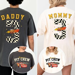 May include: Two oversized t-shirts, one charcoal gray and one cream, feature racing-themed designs. The gray shirt says "DADDY" above a checkered number 3 with "95" and a lightning bolt. The cream shirt says "MOMMY" with a similar design.