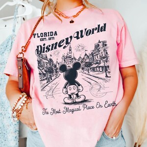 Puede incluir: Camiseta rosa claro con una ilustraci&oacute;n en blanco y negro de Mickey Mouse frente a una escena de Disney World. El texto dice "Florida Disney World" y "The Most Magical Place On Earth."