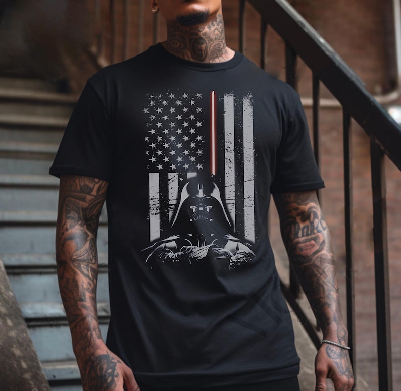May include: Black t-shirt featuring a graphic of Darth Vader's helmet and a lightsaber, integrated into a distressed American flag design. The shirt has a crew neck and short sleeves, suitable for casual wear.