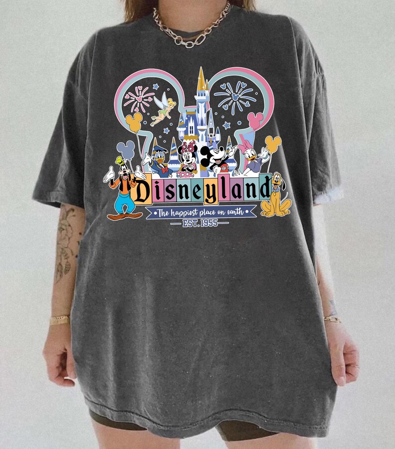 Może przedstawiać: Ciemnoszara koszulka z kolorową grafiką Disneylandu. Projekt zawiera zamek, fajerwerki i r&oacute;żne postacie Disneya. Tekst "Disneyland" jest wyraźnie widoczny, wraz z "The happiest place on earth - EST. 1955."