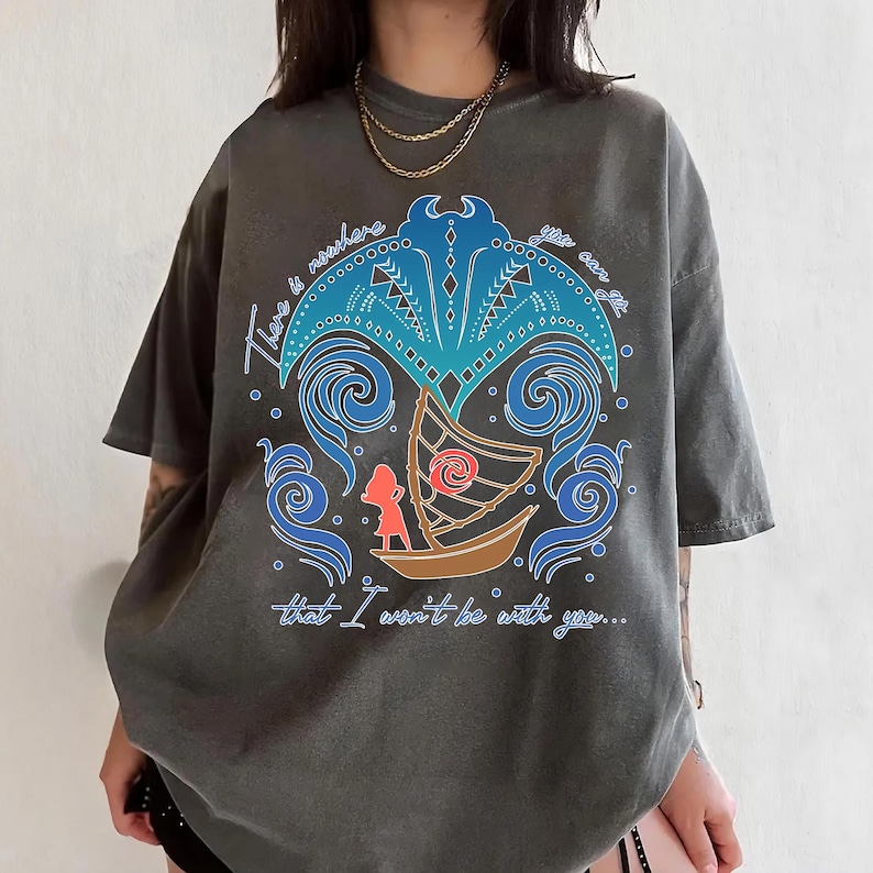 May include: Dark gray t-shirt featuring a colorful graphic design. The design includes a boat, a figure, and stylized waves, with the text "There is nowhere that I won't be with you..."