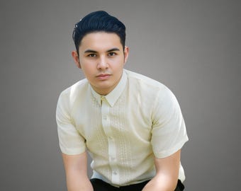 May include: A man wearing a light yellow short-sleeved shirt with a button-up collar and black pants. He is looking directly at the camera.