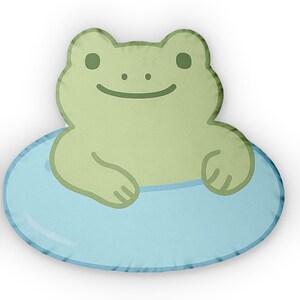 Könnte beinhalten: Ein grünes Plüsch-Froschspielzeug, das auf einem blauen und weißen aufblasbaren Ring sitzt. Der Frosch hat ein lächelndes Gesicht und geschlossene Augen.