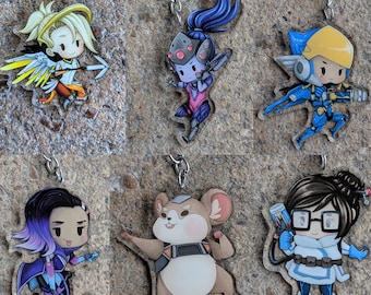 Puede incluir: Conjunto de seis llaveros coloridos con personajes de dibujos animados. Los personajes incluyen un robot rosa y azul, un robot amarillo y azul, una niña rosa y azul con una pistola, una niña amarilla y azul con un arco y flechas, una niña morada y azul con una espada y un hámster marrón y blanco.