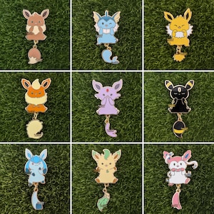 May include: Nine colorful enamel pins featuring various cartoon characters. Each pin has a gold-colored outline and a dangling charm. The characters are in shades of brown, blue, yellow, orange, purple, and black, set against a green background.