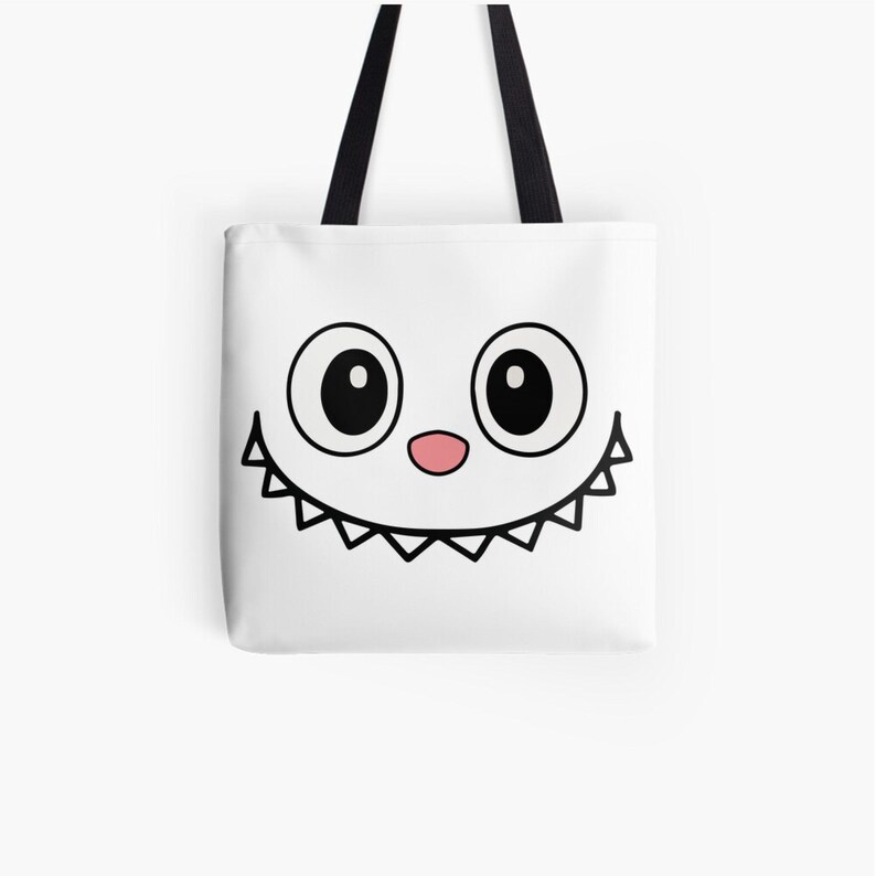 Puede incluir: Bolso tote blanco con un dise&ntilde;o de cara de dibujos animados. Presenta ojos negros grandes, una nariz rosa y una sonrisa dentada. El bolso tiene asas negras y est&aacute; dise&ntilde;ado para transportar objetos.