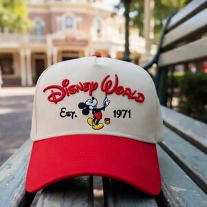 Op de afbeelding: Een baseballcap met een rode klep en een cr&egrave;mekleurige kroon. De cap heeft de woorden "Disney World" in het rood, samen met een afbeelding van Mickey Mouse en het jaar "1971".