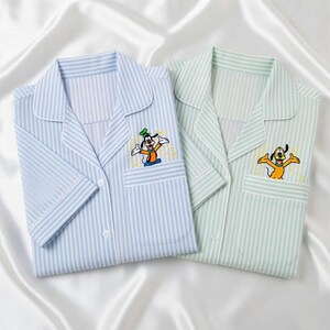 May include: Two pajama tops, one light blue and one mint green, both with vertical stripes. Each has a chest pocket and a cartoon character embroidered on it. The light blue top features Goofy, and the green top features Pluto.