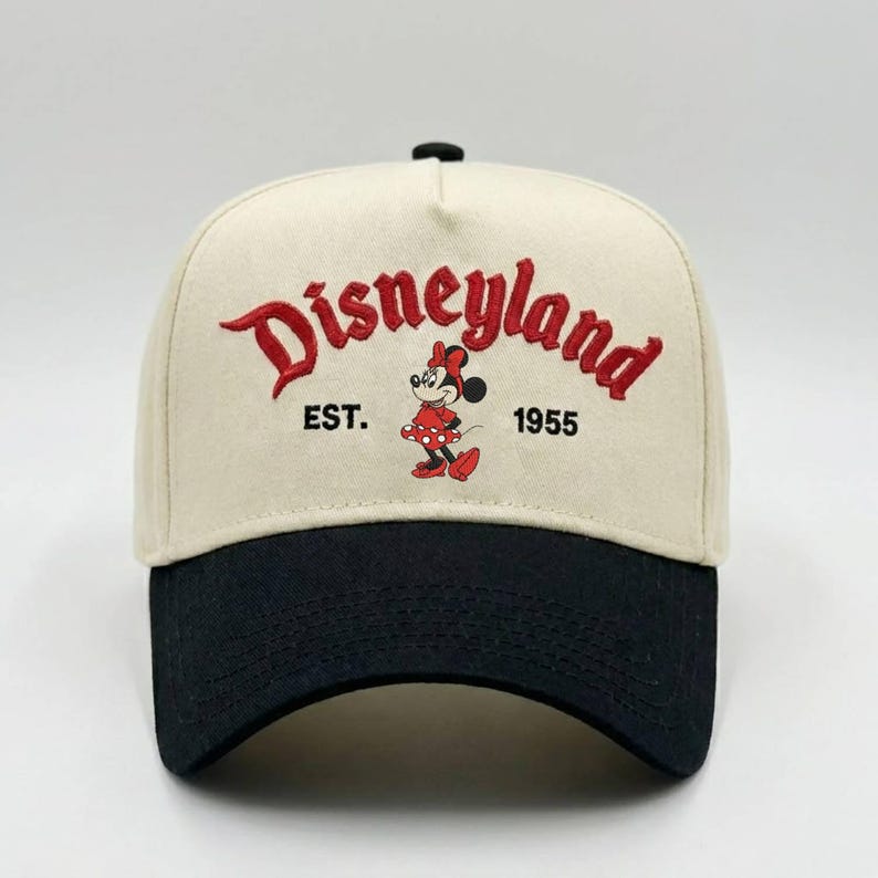 May include: A beige and black baseball cap featuring the word "Disneyland" in red script. The cap also includes the text "EST. 1955" and a Minnie Mouse graphic. The cap has a curved brim and a black button on top.