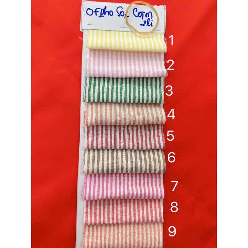 May include: A fabric swatch card featuring nine striped fabric samples in various colors, including yellow, pink, green, and brown. The samples are arranged vertically, with a label at the top that reads "Of pho So.. Com li".