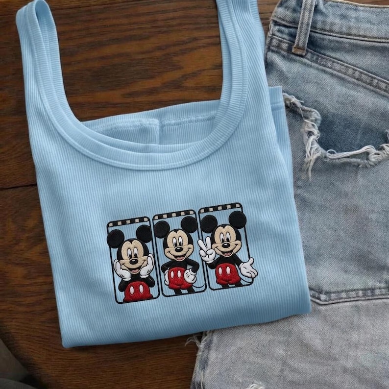 Puede incluir: Una camiseta sin mangas azul claro con tres im&aacute;genes de Mickey Mouse en marcos negros. Mickey se representa en varias poses con pantalones cortos rojos y guantes blancos. La camiseta sin mangas se combina con pantalones cortos de mezclilla.