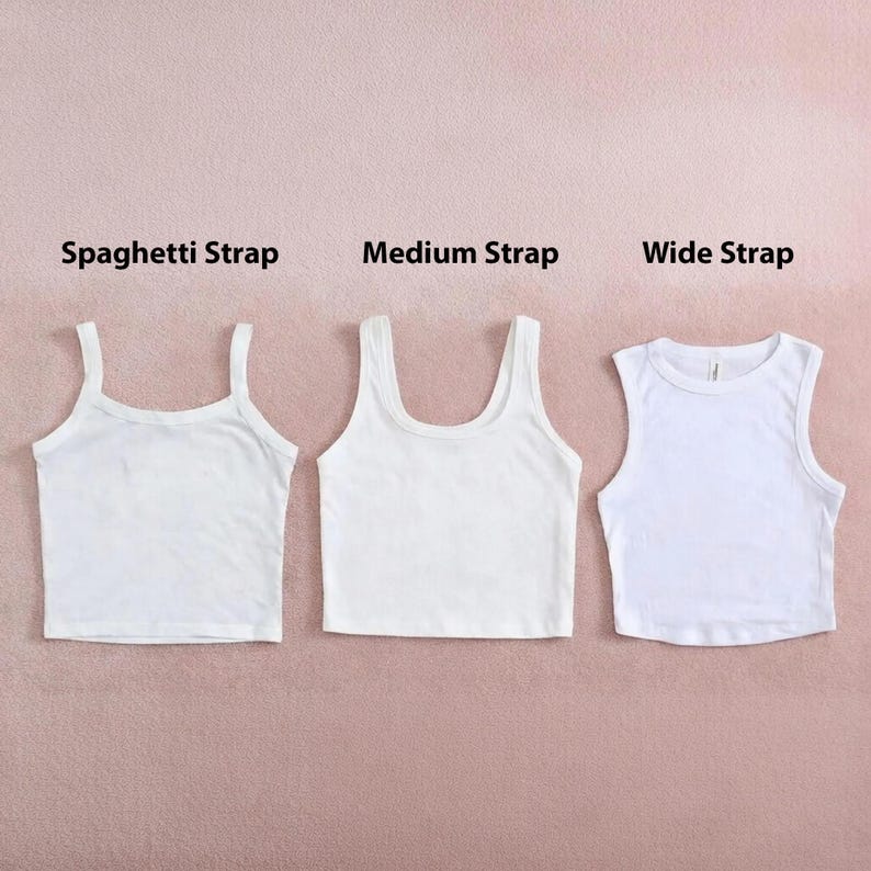 Op de afbeelding: Drie witte crop tops met verschillende bandjes worden getoond tegen een roze achtergrond. De stijlen zijn gelabeld: Spaghetti Strap, Medium Strap en Wide Strap. De tops zijn gemaakt van een zacht materiaal, waarschijnlijk katoen.