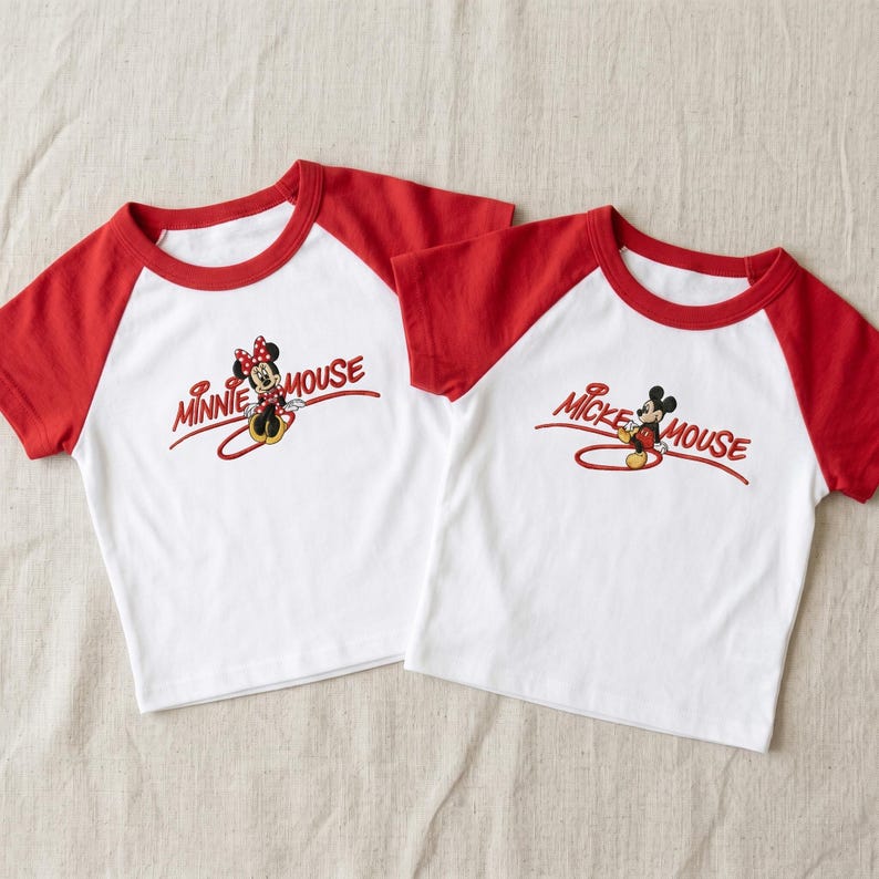 Op de afbeelding: Twee witte t-shirts met rode raglanmouwen. Het linker t-shirt heeft een afbeelding van Minnie Mouse en de tekst MINNIE MOUSE. Het rechter t-shirt heeft een afbeelding van Mickey Mouse en de tekst MICKEY MOUSE. Beide shirts hebben een ronde hals.