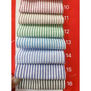 May include: A stack of fabric swatches in various colors, each with vertical stripes. Colors include red, brown, green, blue, and gray. The swatches are numbered 10 through 16, indicating different fabric options for textiles or clothing.