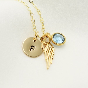 以下が含まれることがあります： 小さな丸いチャームに「F」の文字が刻まれたゴールドネックレス。小さなエンジェルウィングチャームとライトブルーのジェムストーンチャームが付いています。