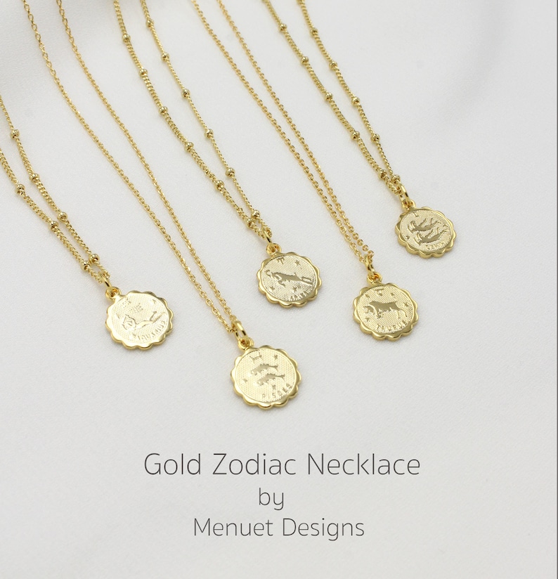 May include: Five gold necklaces with zodiac signs on the pendants. The signs are: Sagittarius, Taurus, Leo, Capricorn, and Pisces. The necklaces are on a white background. Gold Zodiac Necklace by Menuet Designs.