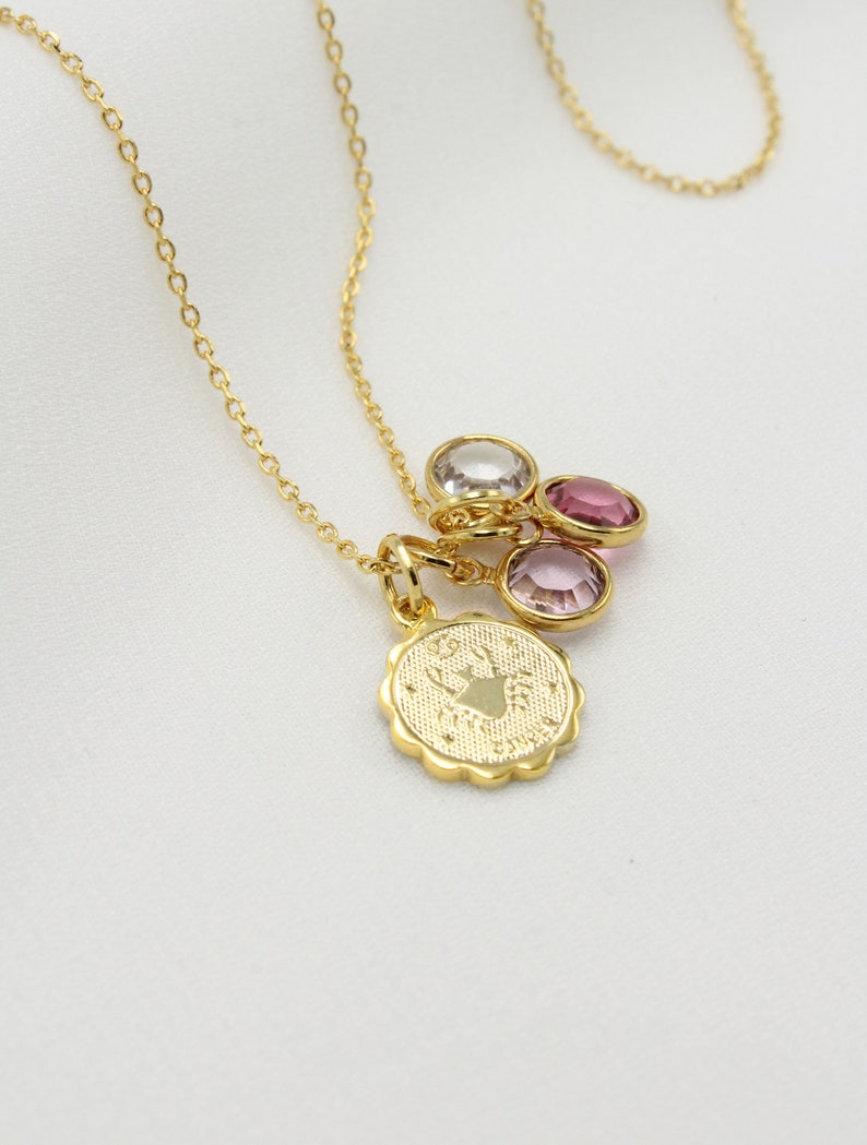 May include: Gold chain necklace with a charm featuring a zodiac symbol and three small pink and clear gemstones.
