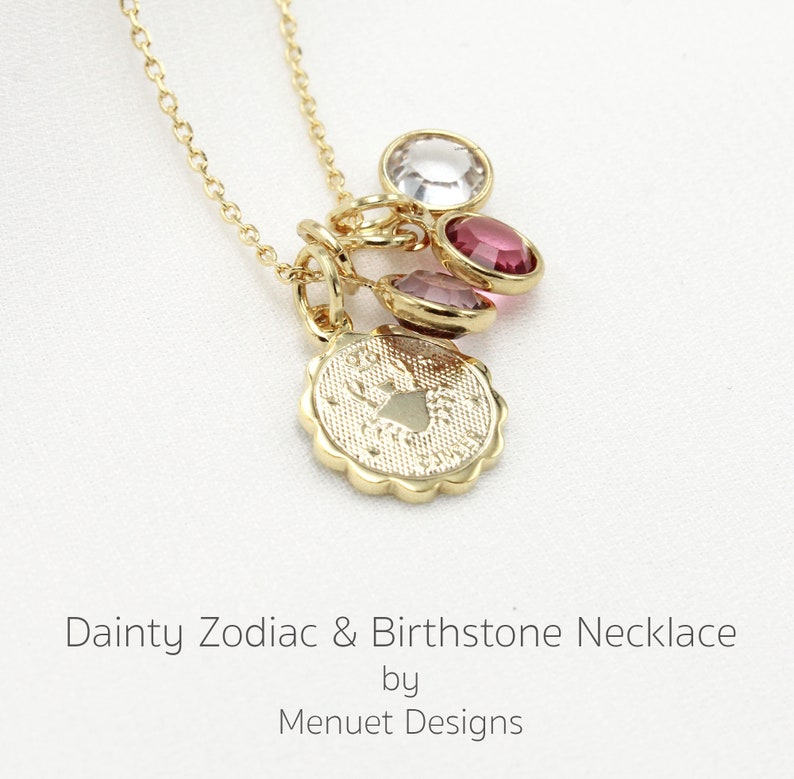 May include: Gold necklace with a zodiac charm and three birthstone charms. The zodiac charm is a crab, representing the Cancer sign. The birthstones are clear, pink, and red.