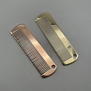 May include: Two rectangular metal combs with fine teeth, one in a polished rose gold finish and the other in a polished yellow gold finish. Each comb features a rounded top edge and a small circular hole at the bottom corner for hanging or attachment.