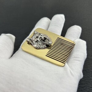 May include: A rectangular comb with a silver wolf head on a gold-colored base. The comb has thin, parallel teeth. The wolf head is detailed with fur and facial features.