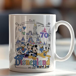May include: White ceramic mug featuring a colorful Disneyland design. The design includes Mickey Mouse, Donald Duck, and other characters in front of a castle, with the text "Disneyland" and "70 Magical Year".