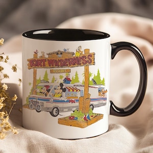 May include: White ceramic mug with a black interior and handle. The mug features a colorful illustration of a van with Mickey and Minnie Mouse, and the text "FORT WILDERNESS RESORT" on a wooden sign. The mug is decorated with cartoon characters and trees.