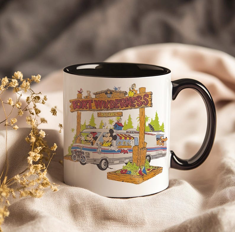 May include: White ceramic mug with a black interior and handle. The mug features a colorful illustration of a van with Mickey and Minnie Mouse, and the text "FORT WILDERNESS RESORT" on a wooden sign. The mug is decorated with cartoon characters and trees.