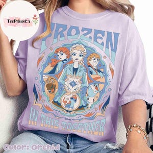 K&ouml;nnte beinhalten: Orchideenfarbenes T-Shirt mit einem Grafikdesign aus dem Film "Frozen". Das Design zeigt die Charaktere Elsa, Anna, Kristoff, Olaf und Sven, mit den Worten "FROZEN" und "IN THIS TOGETHER". Das Shirt hat eine lockere Passform.