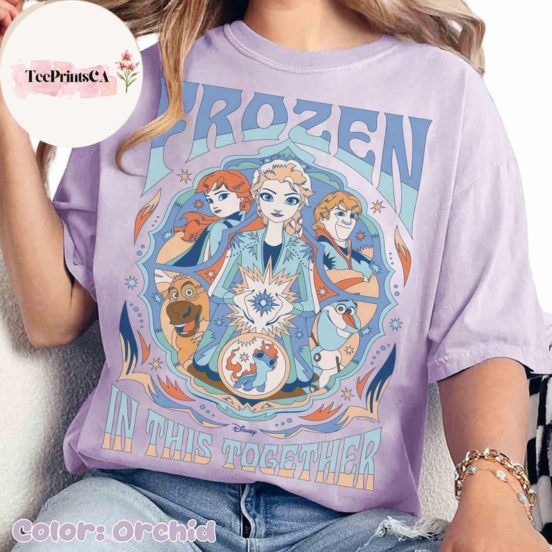 K&ouml;nnte beinhalten: Orchideenfarbenes T-Shirt mit einem Grafikdesign aus dem Film "Frozen". Das Design zeigt die Charaktere Elsa, Anna, Kristoff, Olaf und Sven, mit den Worten "FROZEN" und "IN THIS TOGETHER". Das Shirt hat eine lockere Passform.