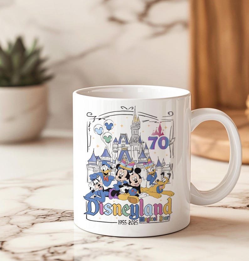 May include: White ceramic mug featuring a Disneyland design. The design includes Mickey Mouse, Donald Duck, Goofy, and a castle, with the text "Disneyland" and "1955-2025 Magical Year". The mug has a curved handle and is suitable for hot or cold beverages.
