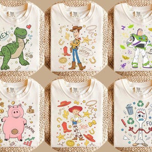 May include: Six off-white t-shirts with cartoon character designs. Each shirt features a different character: Rex the dinosaur, Woody the cowboy, Buzz Lightyear, Hamm the pig, Jessie the cowgirl, and Forky. The designs are in various colors.