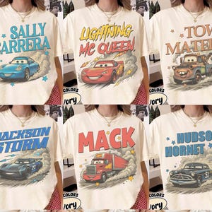 May include: Cream-colored t-shirts featuring various characters from the movie Cars. Designs include Sally Carrera, Lightning McQueen, Tow Mater, Jackson Storm, Mack, and Hudson Hornet, each with a corresponding car illustration.