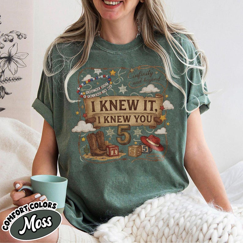 May include: A moss green short-sleeve t-shirt featuring a graphic print with a scroll banner that reads I KNEW IT, I KNEW YOU, the number 5, cowboy boots, a red hat, alphabet blocks, stars, clouds, and the text YOU'VE GOT A FRIEND IN ME.