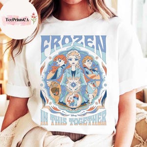 K&ouml;nnte beinhalten: Wei&szlig;es T-Shirt mit einem farbenfrohen Grafikdesign aus dem Disney-Film "Frozen". Das Design enth&auml;lt das Wort "FROZEN" in Blau, zusammen mit Bildern von Charakteren und dem Satz "IN THIS TOGETHER".