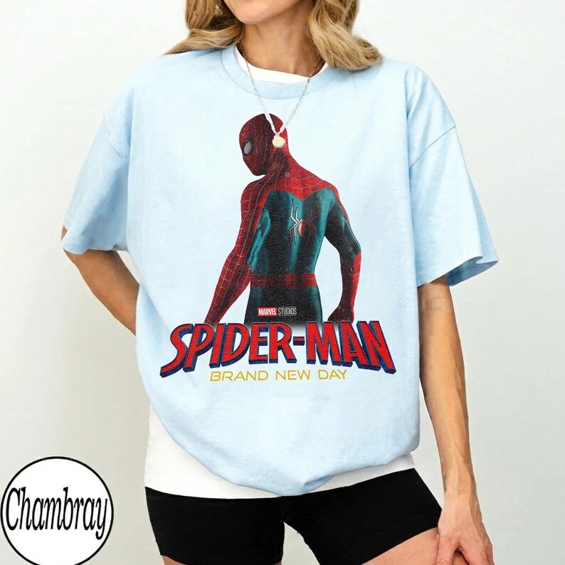 May include: Light blue t-shirt featuring a graphic of Spider-Man in a red and teal suit. The words "SPIDER-MAN" in red and blue are below the image, with "BRAND NEW DAY" underneath.