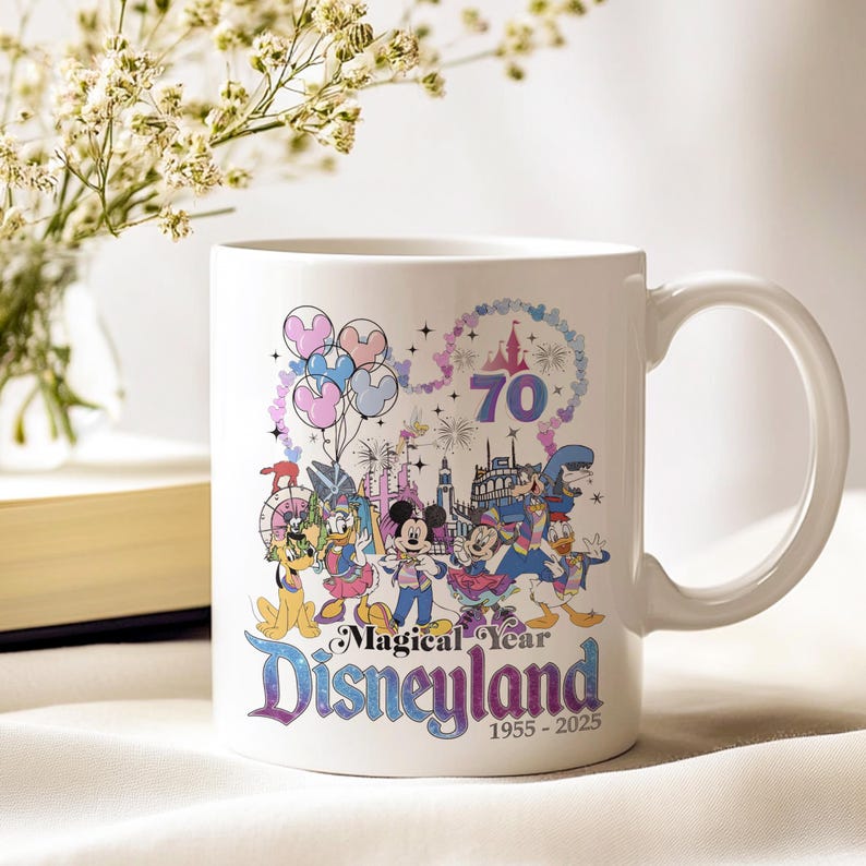 Puede incluir: Taza de cer&aacute;mica blanca con un dise&ntilde;o colorido del 70 aniversario de Disneyland. El dise&ntilde;o incluye a Mickey Mouse, el Pato Donald y otros personajes de Disney, globos y un castillo. Tambi&eacute;n se puede ver el texto "Magical Year Disneyland 1955-2025".