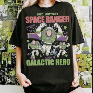 May include: Black t-shirt featuring Buzz Lightyear from Toy Story. The design includes the text "BUZZ LIGHTYEAR'S SPACE RANGER" and "SPIN GALACTIC HERO" with images of Buzz Lightyear in various poses. The shirt is a casual wear item.