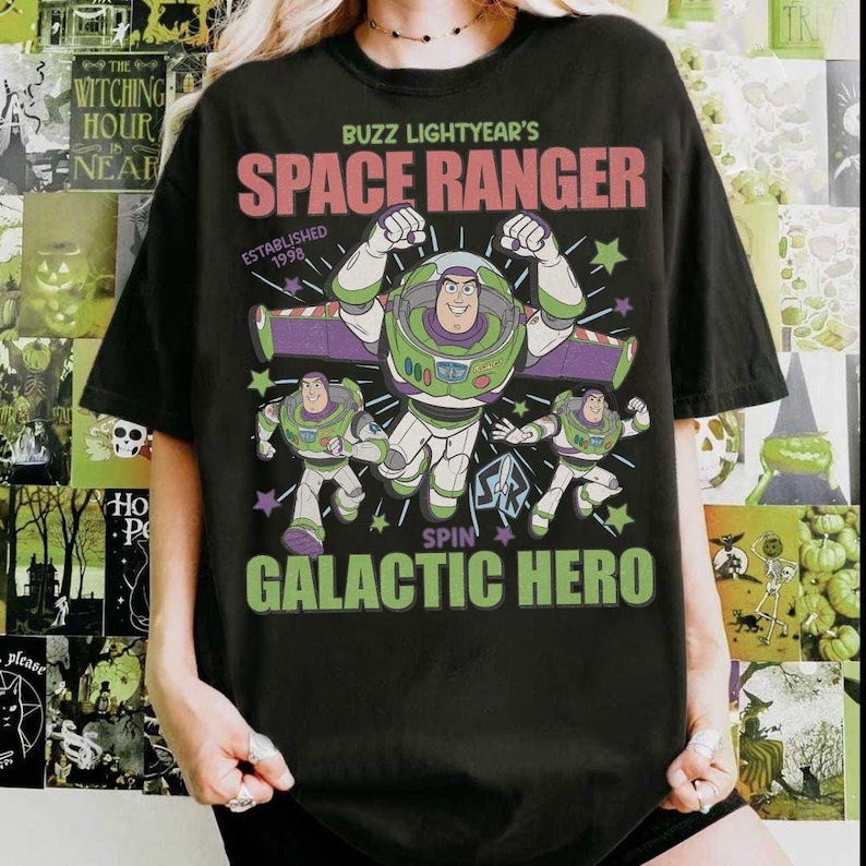 May include: Black t-shirt featuring Buzz Lightyear from Toy Story. The design includes the text "BUZZ LIGHTYEAR'S SPACE RANGER" and "SPIN GALACTIC HERO" with images of Buzz Lightyear in various poses. The shirt is a casual wear item.