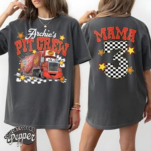 May include: Dark gray t-shirt with the text "Archie's Pit Crew" and a cartoon image of a red truck. The back of the shirt features the word "MAMA", a checkered number 3, and star graphics. The shirt is made of Comfort Colors Pepper material.