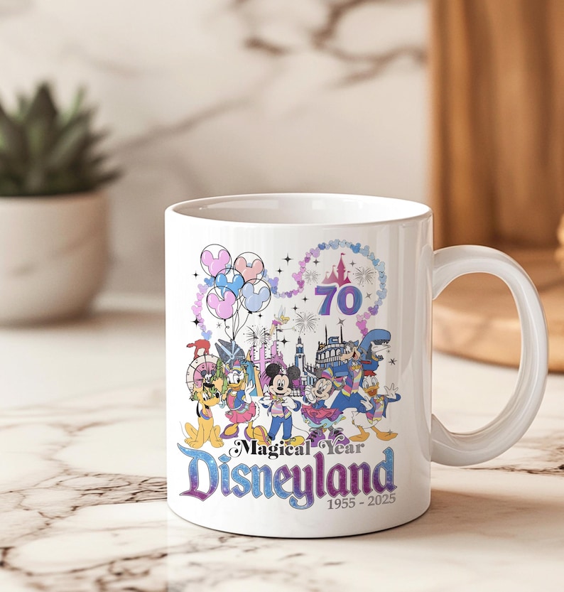 Puede incluir: Taza de cer&aacute;mica blanca con un gr&aacute;fico colorido que celebra el 70 aniversario de Disneyland. El dise&ntilde;o incluye a Mickey Mouse, el Pato Donald y otros personajes, junto con el texto "Magical Year Disneyland 1955-2025."