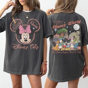 K&ouml;nnte beinhalten: Dunkelgraues T-Shirt mit einem Minnie-Mouse-Design, einer rosa Schleife und dem Text "Disney Trip 2020". Auf der R&uuml;ckseite des Shirts befindet sich eine farbenfrohe Grafik von Disney World mit dem Text "Florida Disney World".