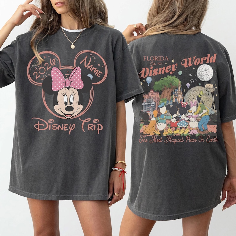 K&ouml;nnte beinhalten: Dunkelgraues T-Shirt mit einem Minnie-Mouse-Design, einer rosa Schleife und dem Text "Disney Trip 2020". Auf der R&uuml;ckseite des Shirts befindet sich eine farbenfrohe Grafik von Disney World mit dem Text "Florida Disney World".